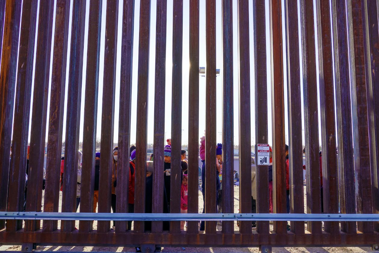 2023年1月4日，美国德克萨斯州埃尔帕索，来自尼加拉瓜和厄瓜多尔的移民站在边境墙上的一扇门旁，等待美国边境巡逻队接走。