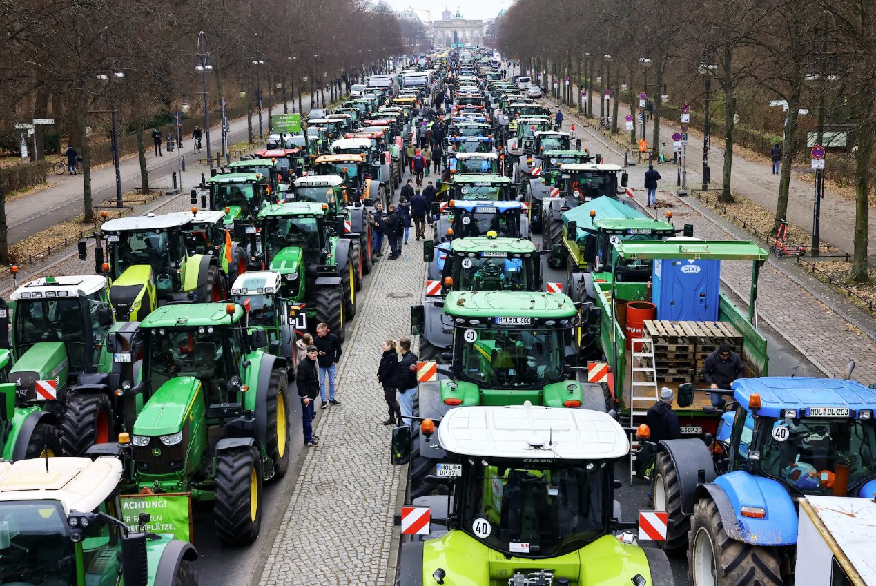2023年12月18日，德国柏林勃兰登堡门附近，德国农民参加反对削减车辆税补贴的抗议活动，人们站在拖拉机旁边。