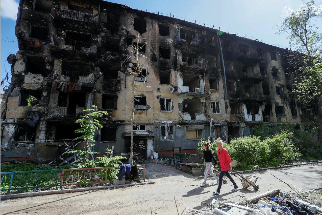 2022年5月20日，乌克兰南部港口城市马里乌波尔，人们走过一栋在乌克兰与俄罗斯冲突期间严重受损的住宅楼。