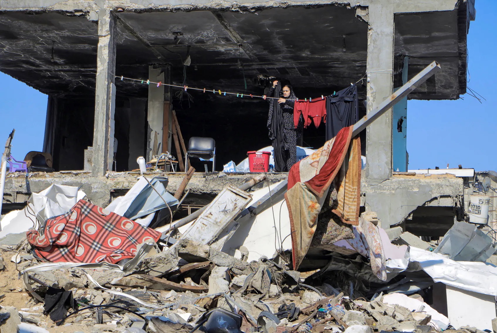 2024年2月22日，在加沙地带北部的贾巴利亚难民营，以色列和哈马斯之间持续不断的冲突中，一名巴勒斯坦人在一座被毁建筑旁挂衣服。