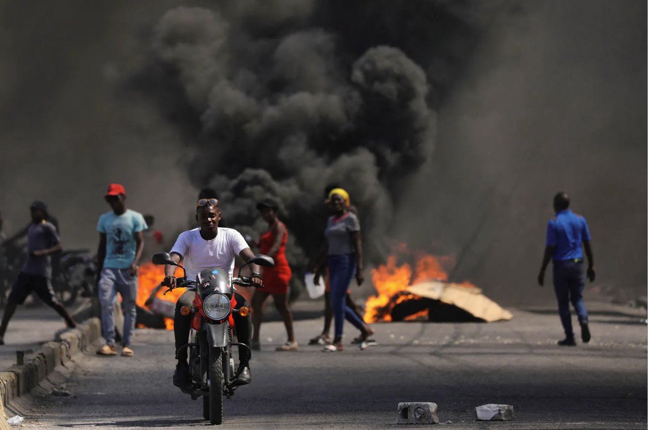 2024年3月1日，海地太子港，一名男子在抗议总理阿里尔·亨利政府和不安全局势的活动中开车经过燃烧的路障。